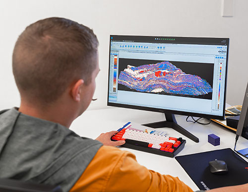 Person sitting at computer. On screen is a mineral map of a core sample.